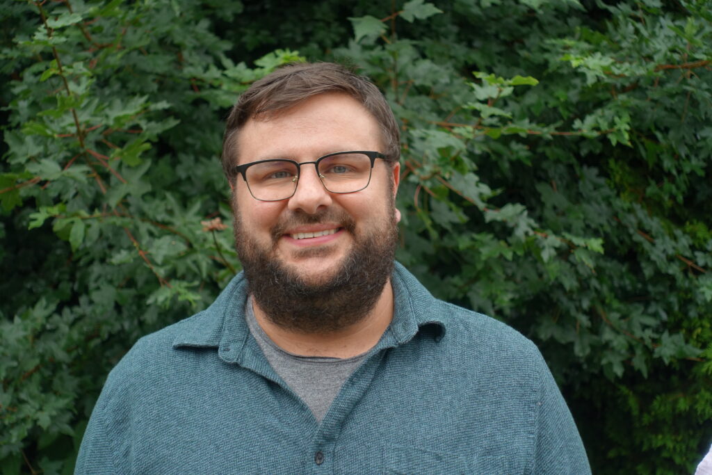 portrait of a man with short brown hair, beard and glasses wearing a green shirt