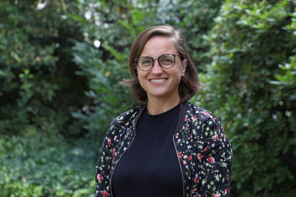 Portrait of a woman with short brown hair and glasses wearing a black shirt and multicolored jacket