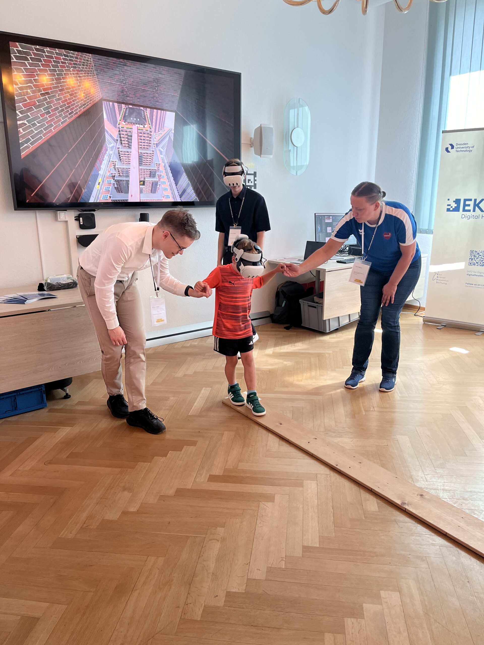 Child is walking over a plank with VR glasses, holding hands on both sides with a woman and a man, assisting him