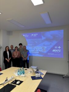 Fünf Personen stehen für ein Gruppenbild vor einer Powerpoint Präsentation