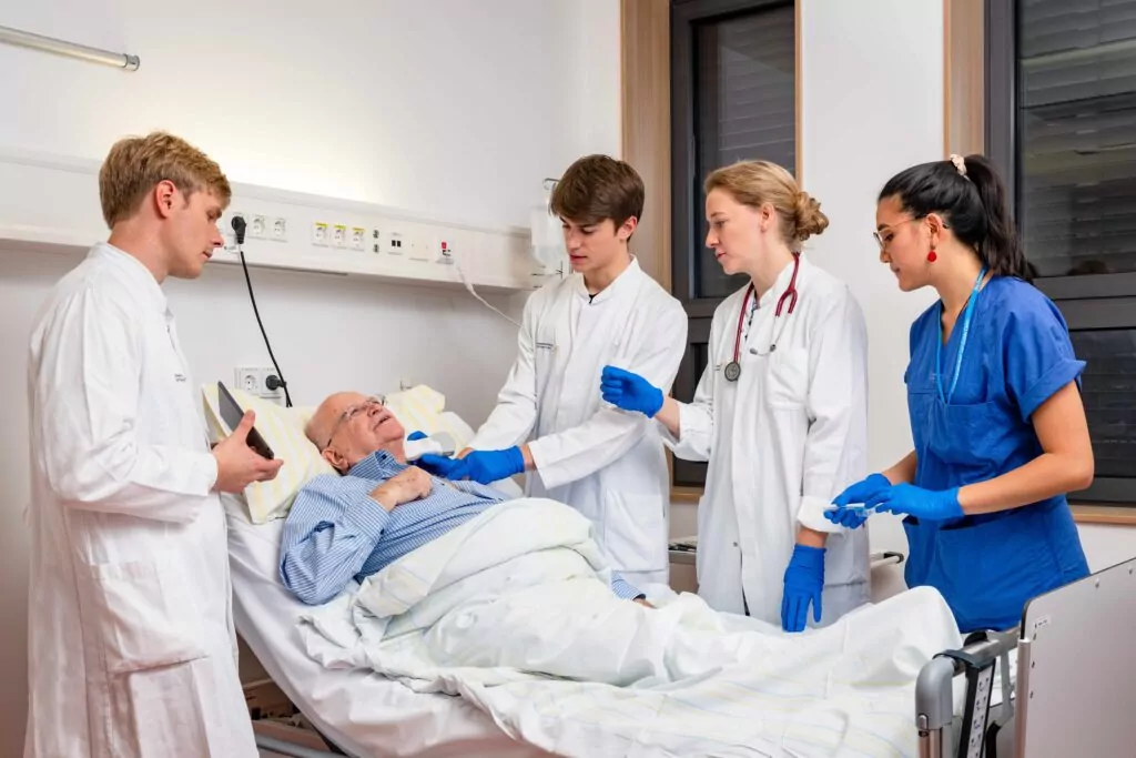 Patient liegt im Bett und Ärzte und Schwester stehen am Bett