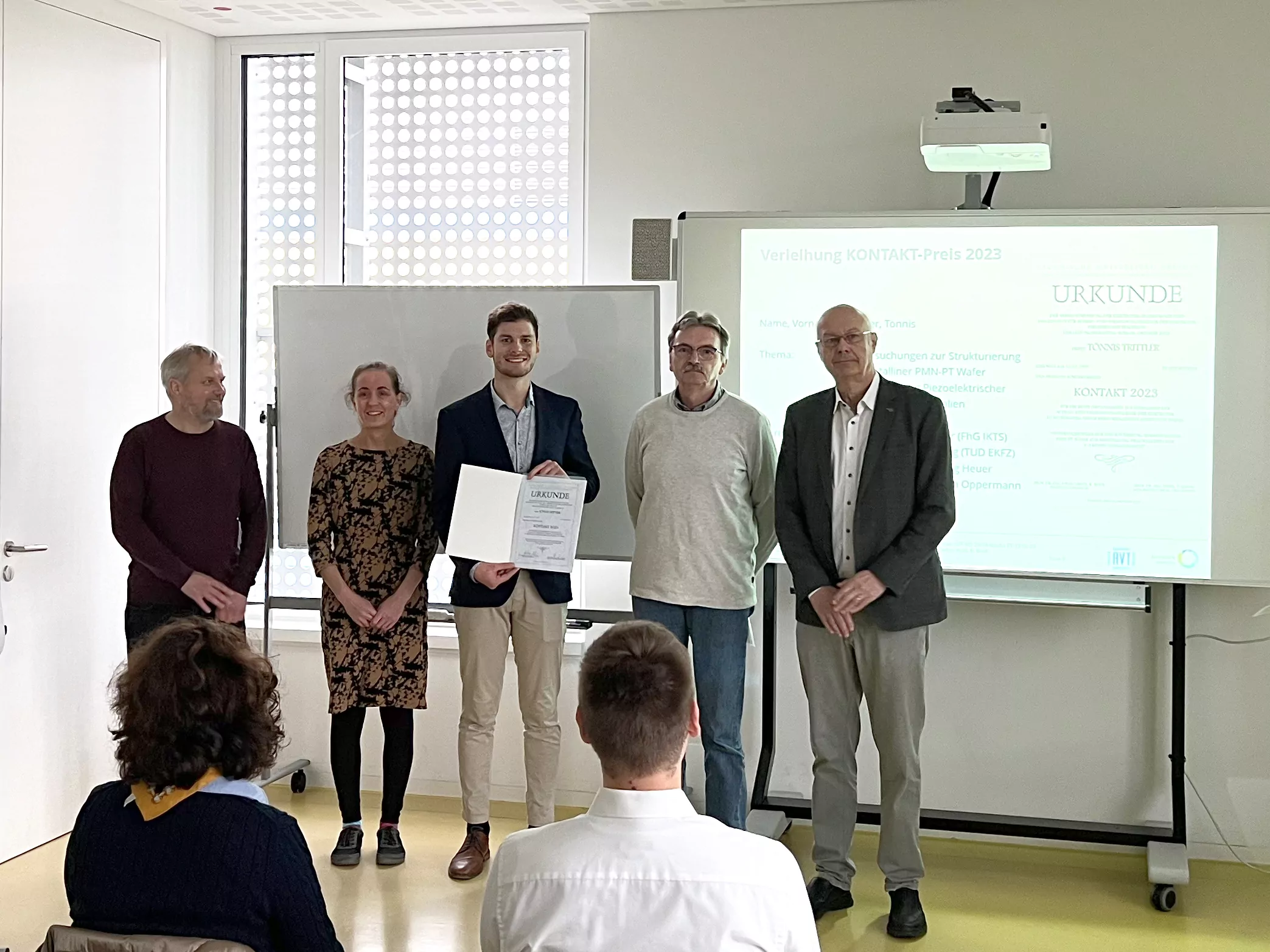 5 people standing in front of an audience. Tönnis in the middle holding the prize