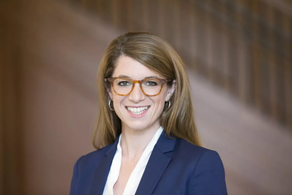 Portrait Ariel D. Stern - a woman with long brown hair wearing glasses and a blue blazer