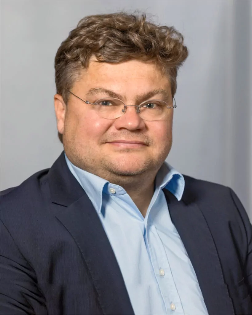 man with curly short hair wearing glasses and a dark blue suit