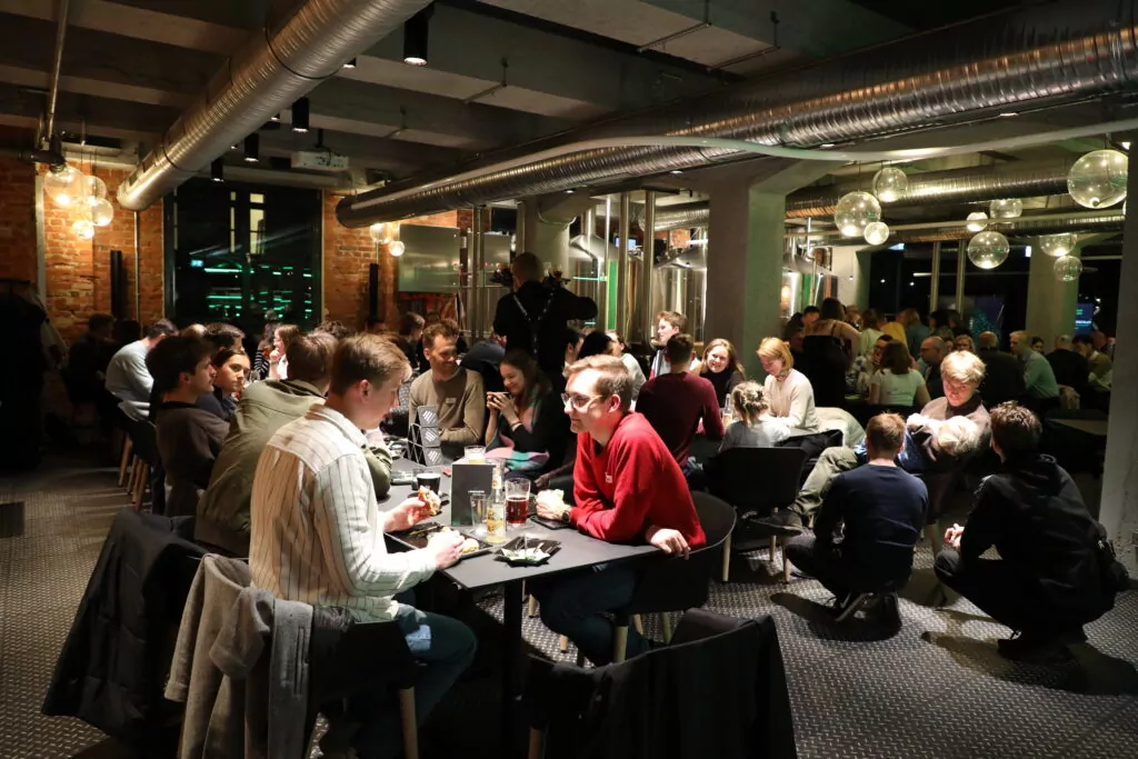 group of people sitting on several tables in bar and talking, the light is dimmed