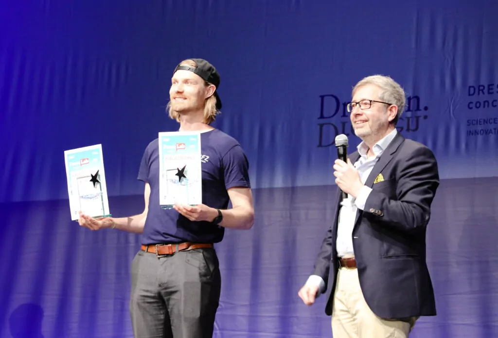 Man with a basecap holding two awards in front of him.