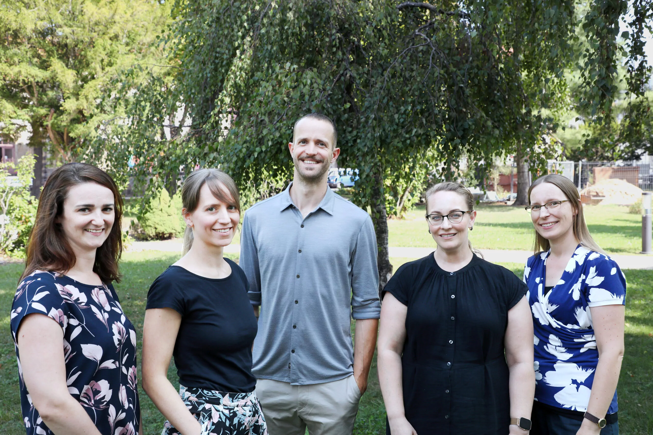 five people, 1 male, 4 females in front of a tree with lawn in the background