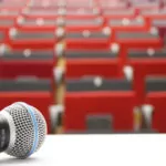 picture of an empty lecture hall with red seats blurry in the background and a microphone lying on the desk in the front