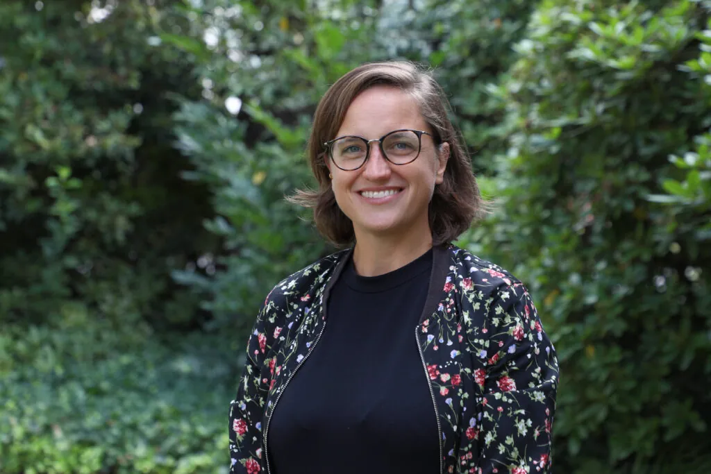Portrait of a woman with short brown hair and glasses wearing a black shirt and multicolored jacket
