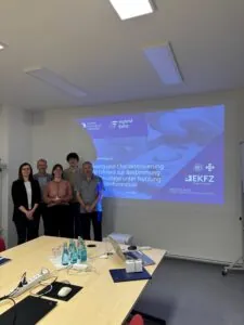 Fünf Personen stehen für ein Gruppenbild vor einer Powerpoint Präsentation